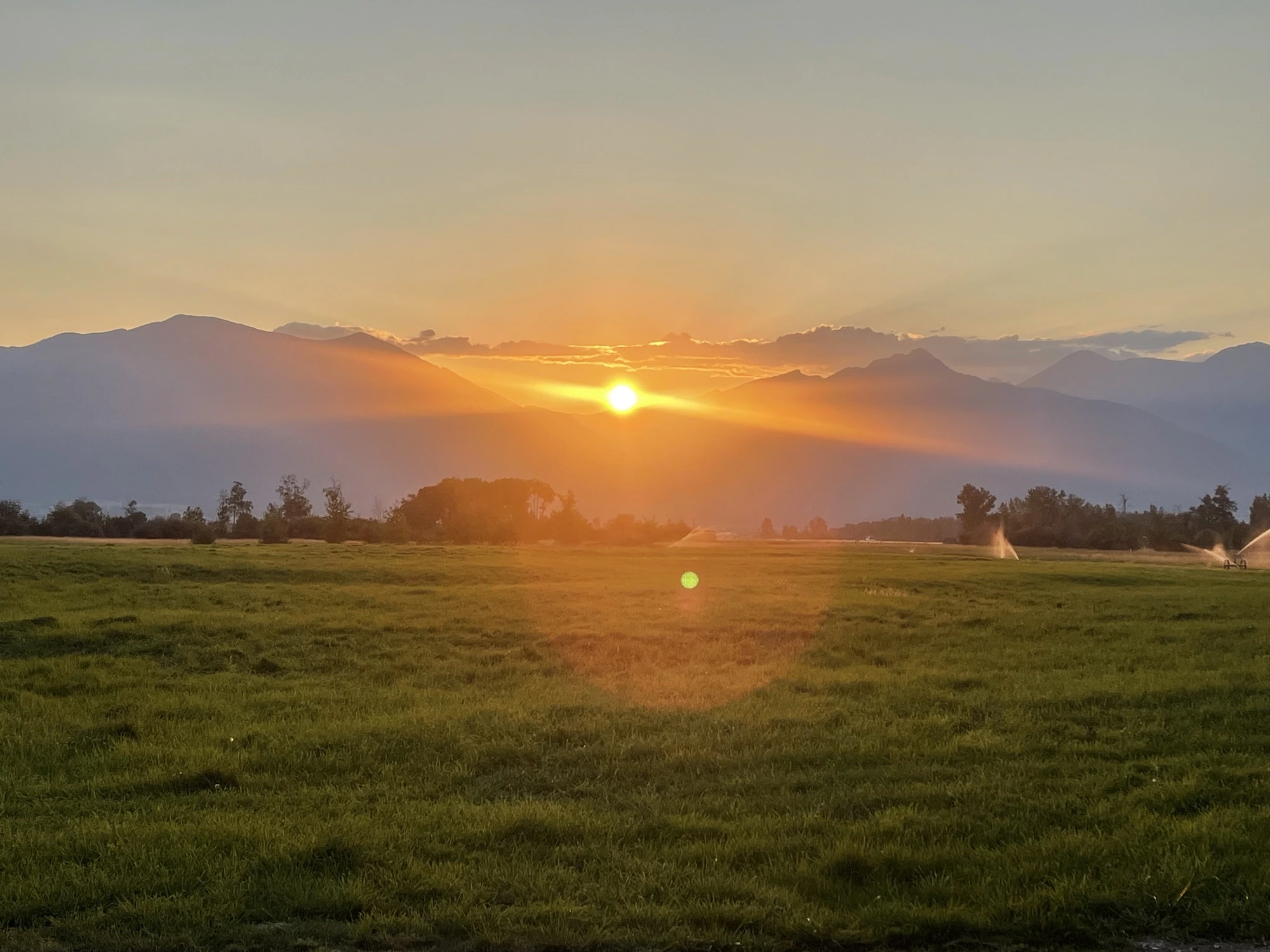 Golden sun cresting the Bitterroot Mountains over the hay field